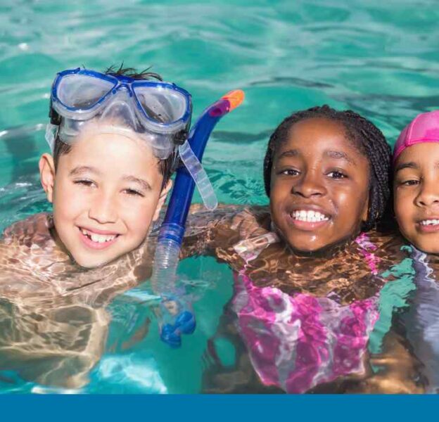 Three smiling children in a pool - a boy wearing a snorkel and mask with two girls
