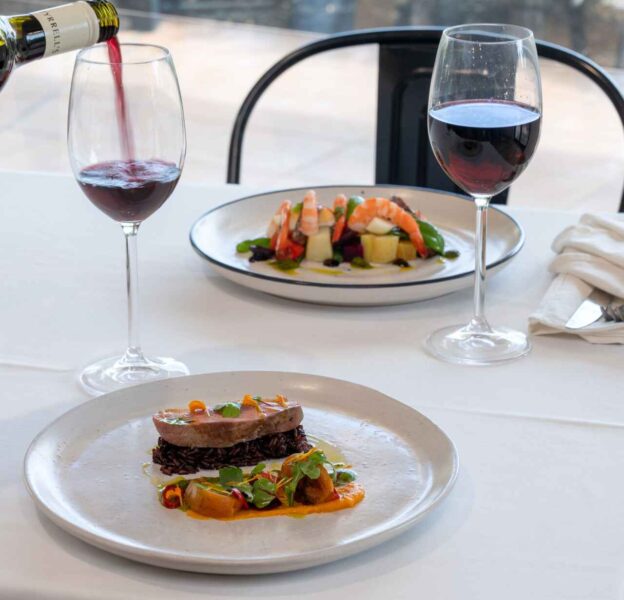 Two plates of appetizers with glasses of red wine on a restaurant table